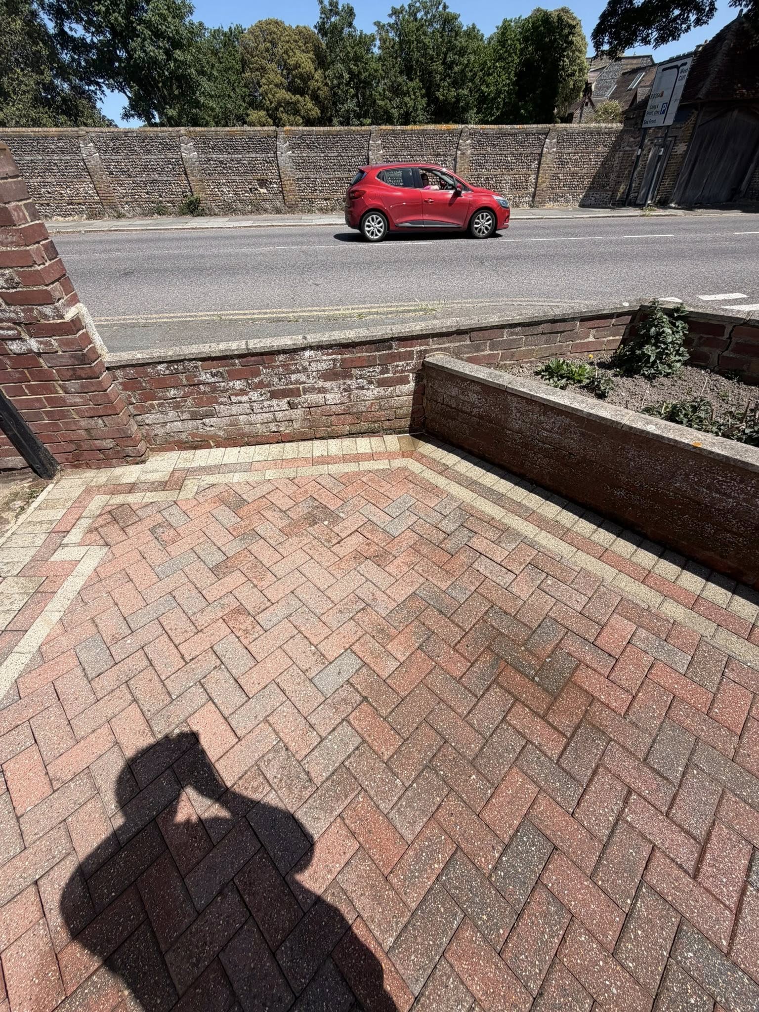 Red car parked on freshly cleaned herringbone brick paving