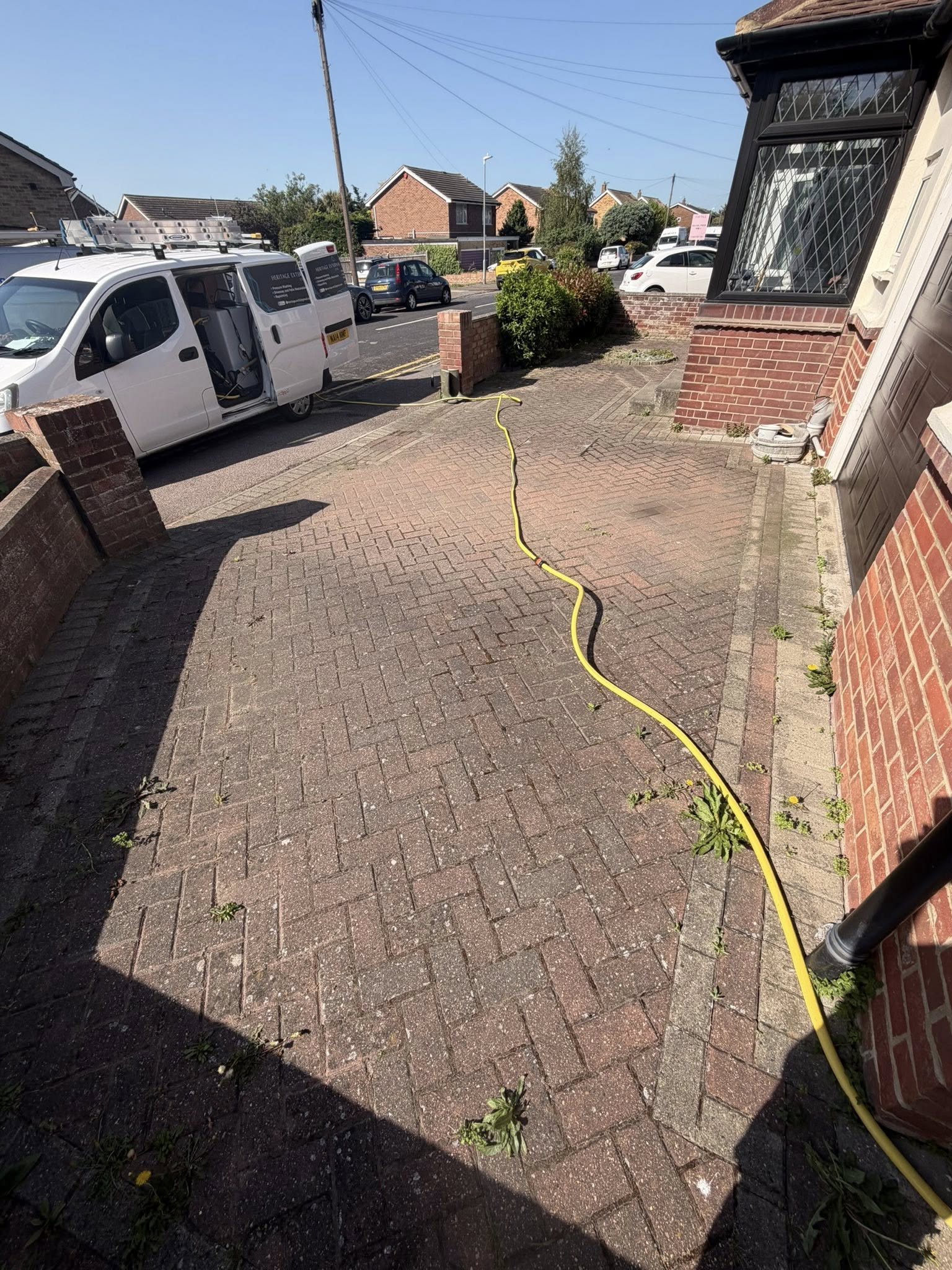 Driveway cleaning in progress with yellow hose